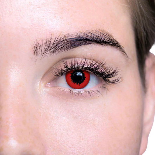Close-up of a person's eye wearing a red contact lens with a black spider-like center and long black eyelashes.