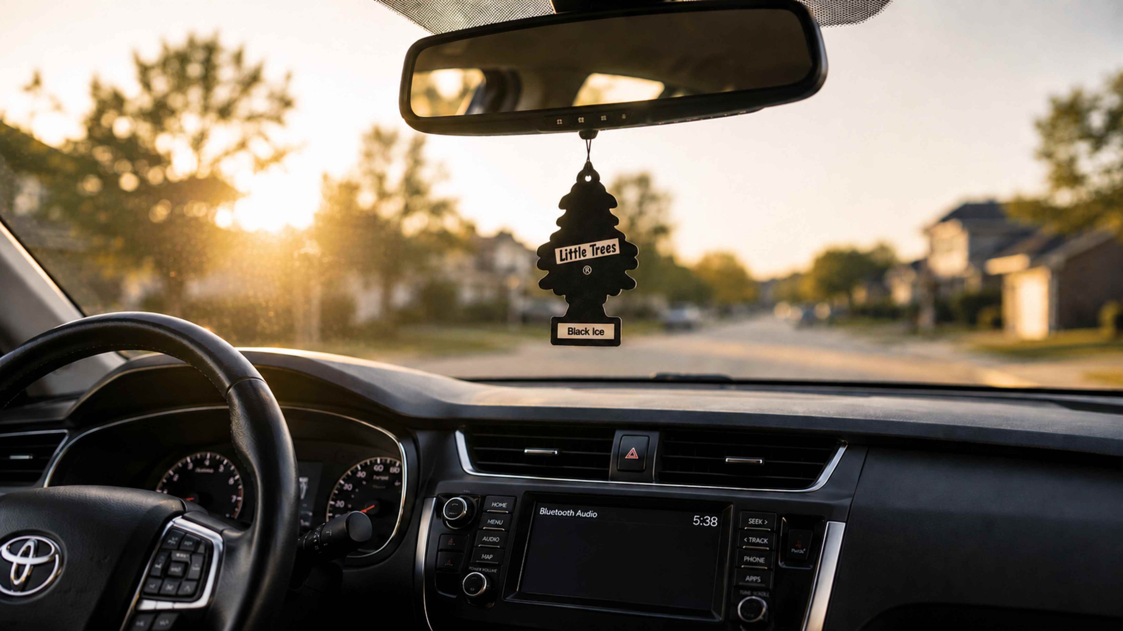Car interior with a rearview mirror hanging air freshener on a blurred suburban street background