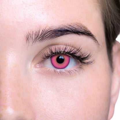 Close-up of a person's eye wearing a bright pink contact lens with a dark pupil and long eyelashes.