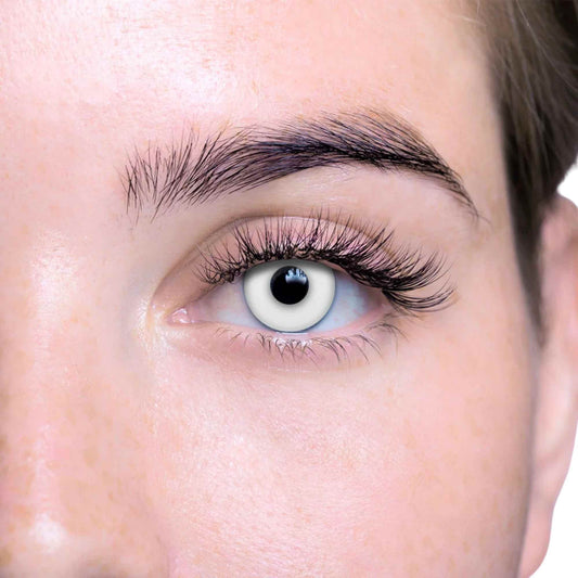 Close-up of a person's eye with white contact lens fitted with long, dark, curled eyelashes and a neatly shaped eyebrow.