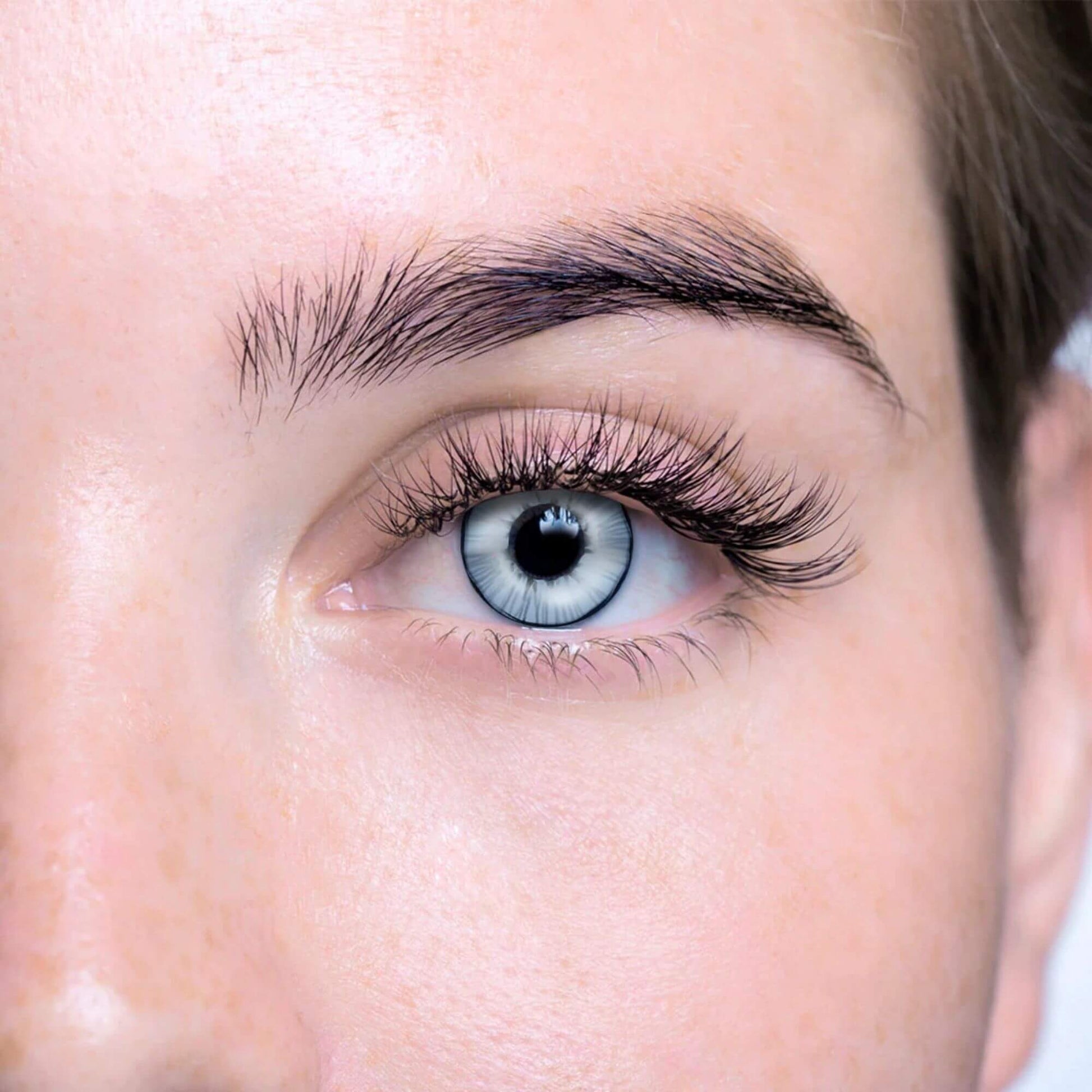 Close-up of a person's eye with white and black contact lens and long eyelashes.