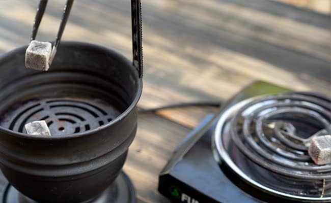 Black portable stove with a pot on top, next to a power adapter on a wooden surface.